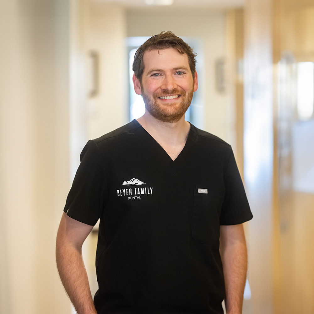 The image shows a man standing in an indoor setting, wearing a black shirt with the word DOCTOR visible on it and a name tag that reads JASON, suggesting he is a medical professional.