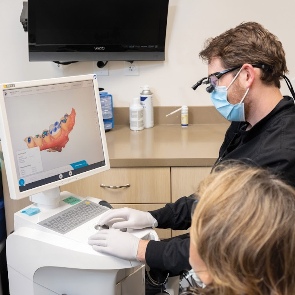 A dental professional is assisting a patient with a digital display of the patient s mouth, highlighting dental work in progress.