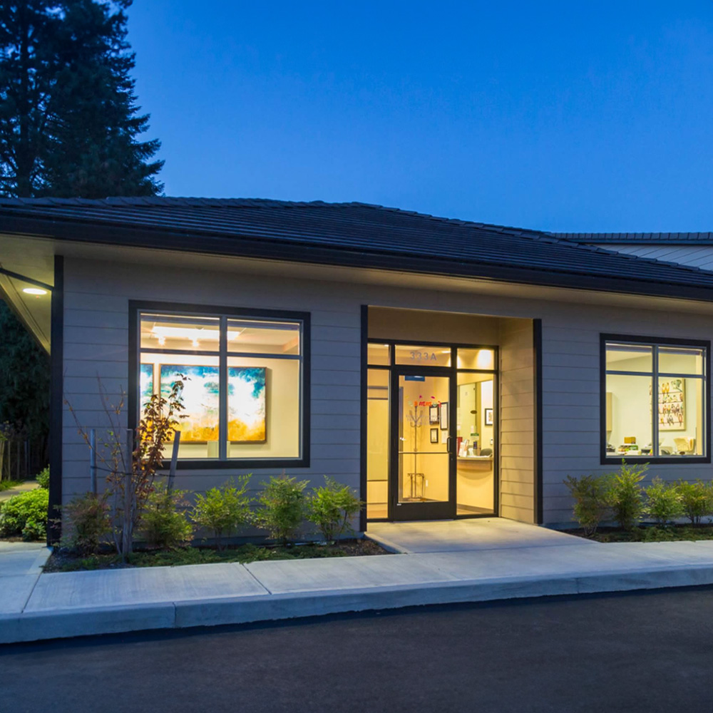 The image depicts a modern building with a flat roof, featuring large windows and a welcoming entrance.